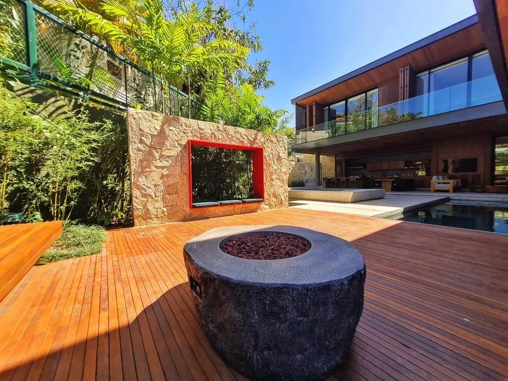 Área externa com fogueira e deck de madeira, cercada de pedra