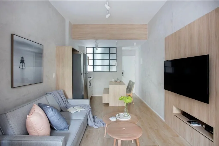 Loft em corredor com sala, TV e cozinha ao fundo