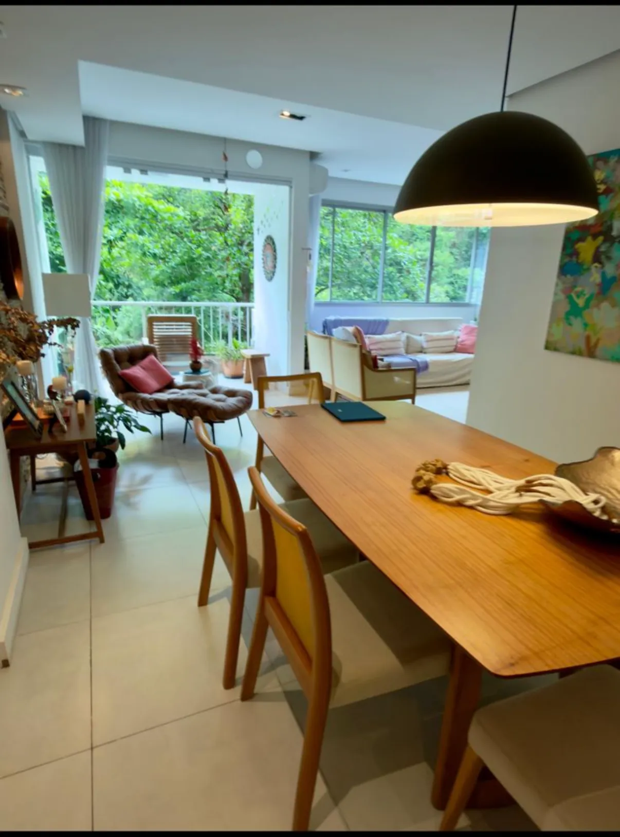 Sala de jantar com mesa de madeira e luminária pendente, ao lado da varanda