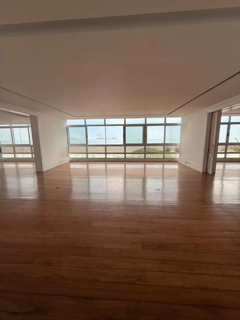 Salão vazio de 480 m², com piso de tacos de madeira e janelas do chão ao teto voltadas para o mar de Ipanema